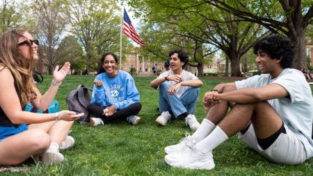 Four students talking and sitting on the lawn of McCorkle Place on the campus of UNC-Chapel Hill